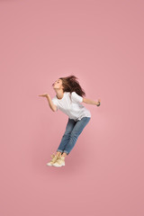 Freedom in moving. Mid-air shot of pretty happy young woman jumping and kissing against pink studio background. Runnin girl in motion or movement. Human emotions and facial expressions concept