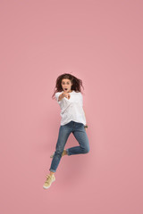 Fototapeta na wymiar Freedom in moving. Mid-air shot of pretty happy young woman jumping and pointing to camera against pink studio background. Runnin girl in motion or movement. Human emotions and facial expressions