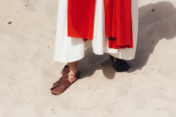 cropped image of Jesus in robe, red sash and sandals standing on sand in desert