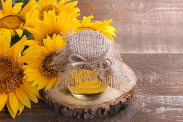 Sunflower oil in a jar on a wooden stand and sunflowers on a brown wooden table with a place for inscription