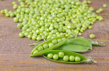 Fresh green peas in a close-up and a pea in the background on a brown wooden table
