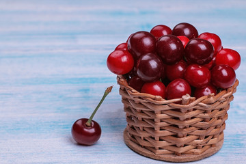 Composition with ripe red cherries in a wicker basket on a blue wooden table.