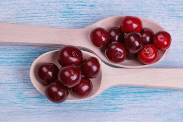 Composition with ripe red cherries in wooden spoons close-up blue wooden table. top view