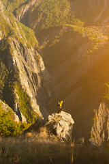 Tourist stands at the edge of the cliff with his dog and looks at the rocky mountains.