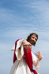 Fototapeta premium low angle view of Jesus having fun and showing two fingers with rosary against blue sky