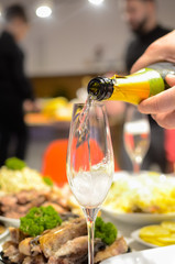 The man fills the glasses with champagne on the christmas table