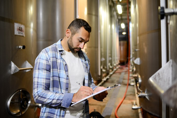 handsome man winemaker in a winery wine cellar during harvest season with stainless steel vats in background - obrazy, fototapety, plakaty