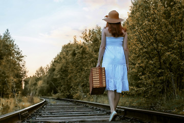 autumn park girl in white sundress and a wicker suitcase walking