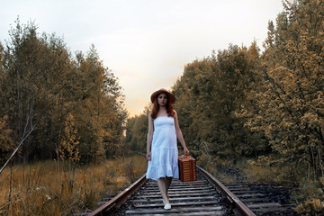 autumn park girl in white sundress and a wicker suitcase walking