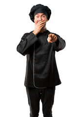 Chef man In black uniform pointing with finger at someone and laughing a lot while covering mouth on isolated white background