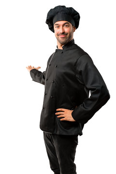 Chef man In black uniform pointing back with the index finger presenting a product on isolated white background