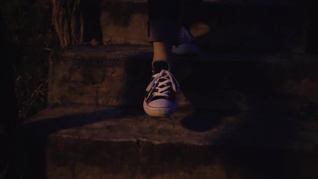 Silhouette of girl legs in sneakers walking downstairs at night in moonlight.