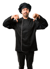 Chef man In black uniform showing thumb down with both hands. Negative expression on isolated white background