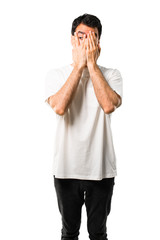 Young man with white shirt covering eyes by hands and looking through the fingers on isolated white background