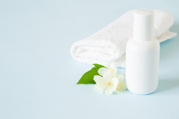 Obraz na płótnie Canvas White bottle of natural herbal shampoo for women with towel on pastel blue table in bathroom. Beautiful jasmine blossoms. Fresh flowers. Care about clean and soft face, hands, legs and body skin.