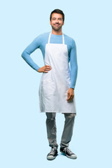Fototapeta premium Full body of Man wearing an apron posing with arms at hip and smiling on blue background