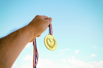 Naklejka na ściany i meble man hand raised, holding gold medal against sky. award and victory concept.