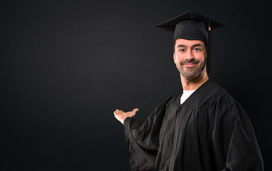 Man on his graduation day University pointing back with the index finger presenting a product on...