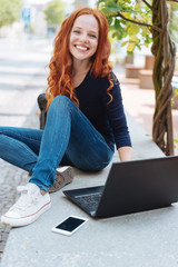 lachende frau sitzt draußen in der stadt und arbeitet am laptop