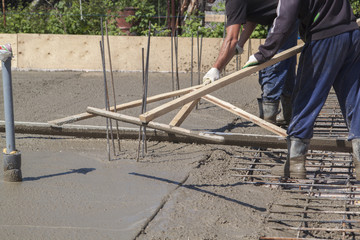 two workers leveling fresh concrete slab with a special wooden working tool
