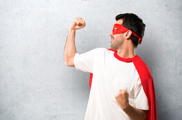 Superhero man with mask and red cape celebrating a victory in winner position on textured grey...