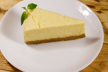 Piece of tasty sweet New York cheesecake in a white plate on wooden table
