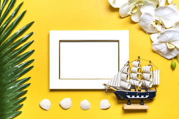 Palm, monstera leaves, orchid, seashells, white photo frame, ship on yellow background. Concept...