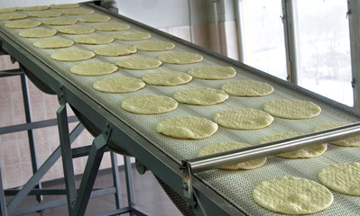 Conveyor with dough, billets for pizza.