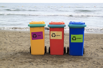 multi-colored containers for sorting garbage are on the beach against the sea