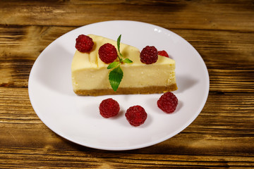 Piece of tasty New York cheesecake with raspberries in a white plate on wooden table
