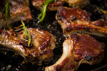 Closeup of Lamb chops frying in a rustic metal pan with rosemary and mixed pepper