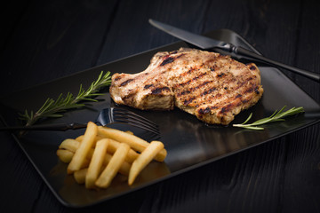 Grilled pork steak on a black plate served with french fries and rosemary