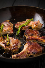Lamb chops frying in a rustic metal pan with rosemary and mixed pepper