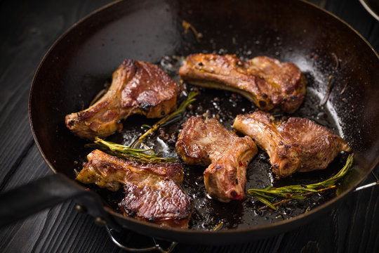 Lamb chops frying in a rustic metal pan with rosemary and mixed pepper