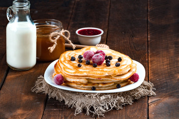 Pancakes with fresh, frozen berries of blueberries and cherries, raspberry jam, milk and honey on a wooden background. Delicious, healthy breakfast