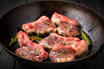 Lamb chops frying in a rustic metal pan with rosemary and mixed pepper