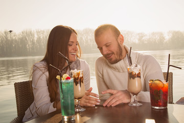 Couple using cellphone and drinking coffee on the river.