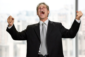 Fototapeta premium Businessman expresses victory with raised hands. Portrait of man in business suit clenched his fists in excitement. Enjoying business triumph.