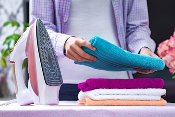 A young housewife in a shirt folds clean towels after ironing on the ironing board. Home routines....
