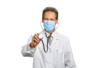 Mature doctor with mask and stethoscope. Smiling caucasian male doctor in mask showing stethoscope. Doctor isolated on white background.