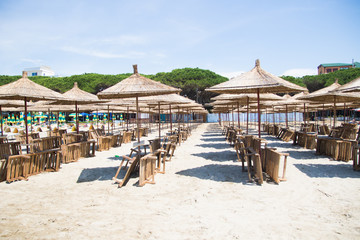 Albania. Golem. Beach shoreline with sun umbrellas made from straw. A blue sky on the Adriatic Sea. - obrazy, fototapety, plakaty