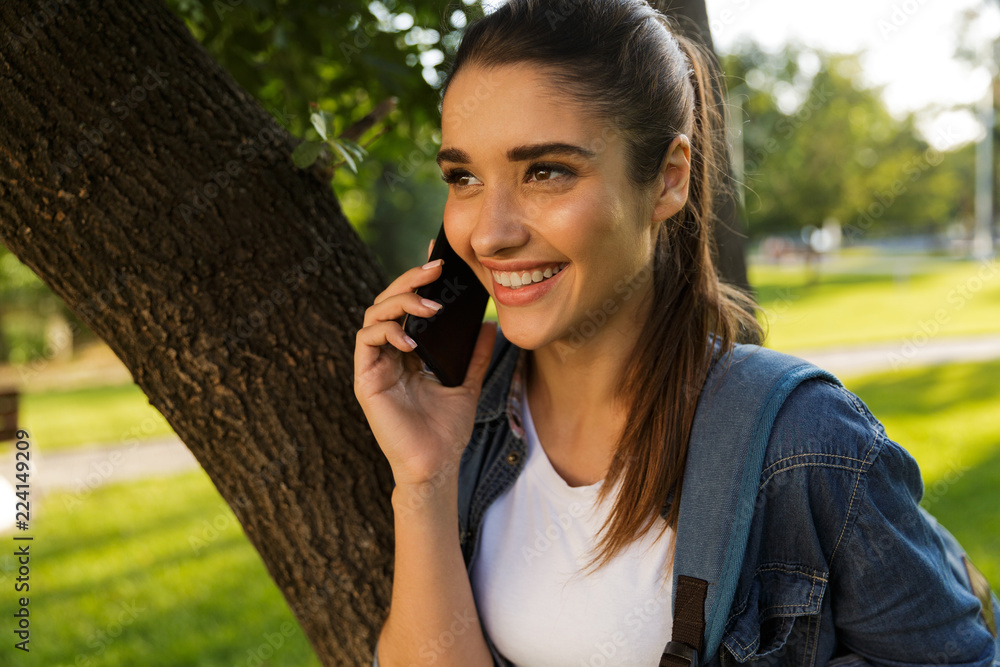 Poster beautiful woman student walking in park talking by mobile phone.