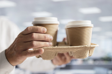 Businessman carrying coffee take out disposable cups in office for meeting