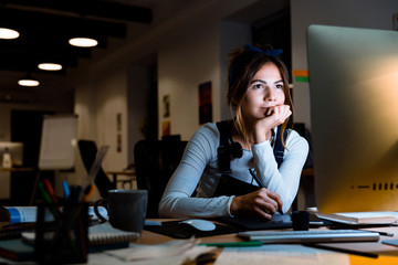 Young woman graphic designer using pc computer working with tablet at night in office.