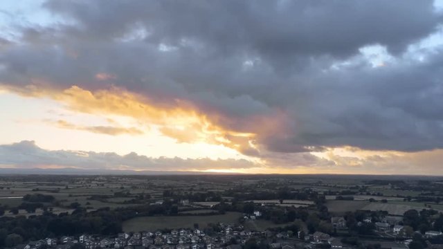 Aerial view, tilt and rise up move. Dramatic rainy sky sunset behind residential area of small town, Tarvin in Cheshire.