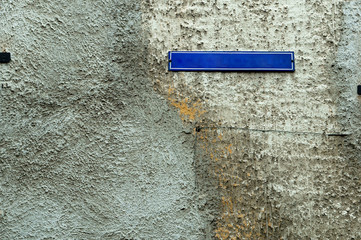 The nameplate on the house on the street. A sign on the stone wall outside on the street.