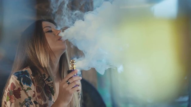 Passionatte woman admiringly smoking e-cigarette in a room. 4K