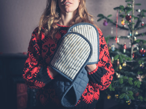 Woman with oven gloves by the christmas tree