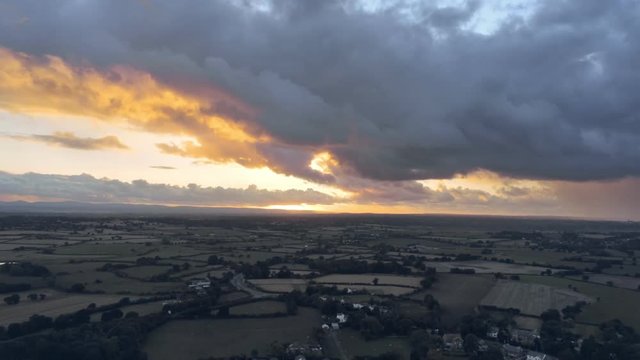 Aerial view, tilt up move. Dramatic fast moving sky and sunset over houses of small town, Tarvin in Cheshire.