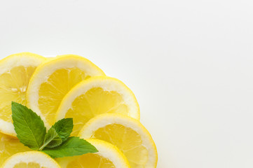 Top view of lemon slices on a round plate with mint leaves - in the corner of image and copy space on rest white background.